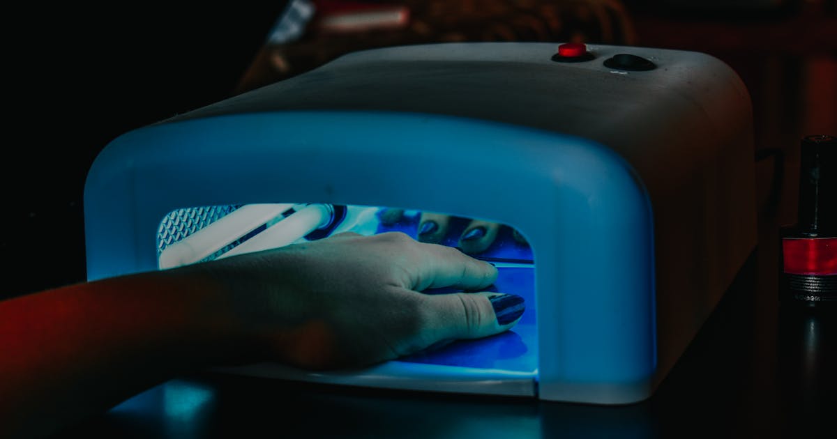 Lámpara UV clásica de tubos fluorescentes con una mano dentro curando las uñas