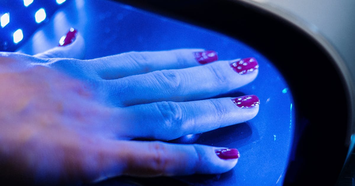 Mano con uñas pintadas de fucsia curando el semipermanente bajo una lámpara LED con luz azul