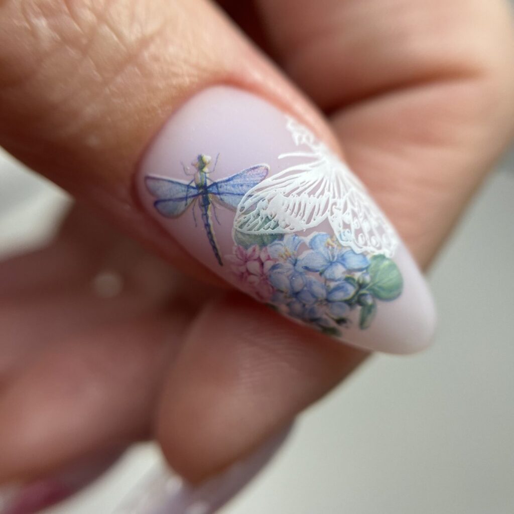 Uña almendrada rosa lechoso con una libélula y flores estampadas en azul y blanco