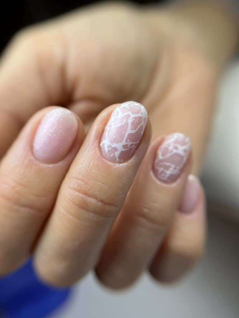 Uñas cortas en rosa pálido con dos uñas decoradas con un dibujo blanco