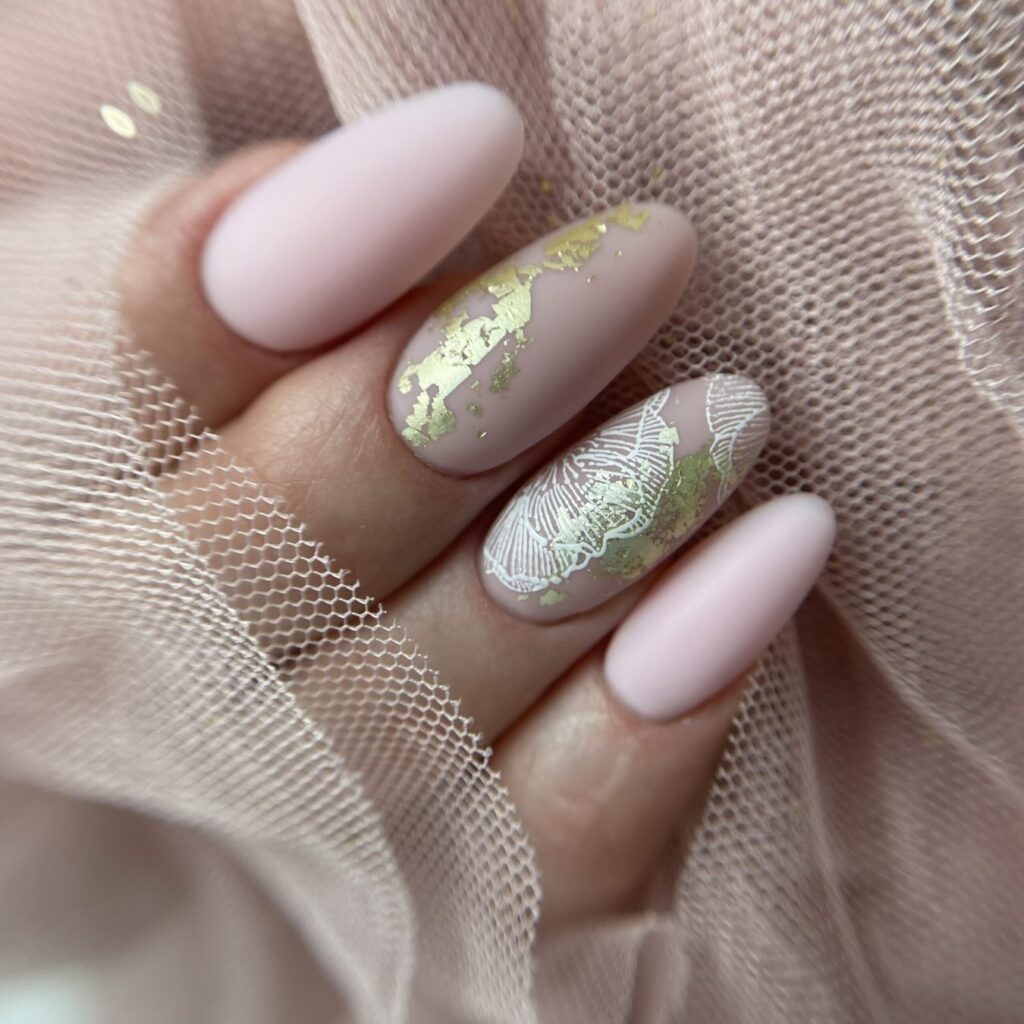 Uñas almendradas en rosa pálido mate con dos uñas decoradas en dorado y blanco