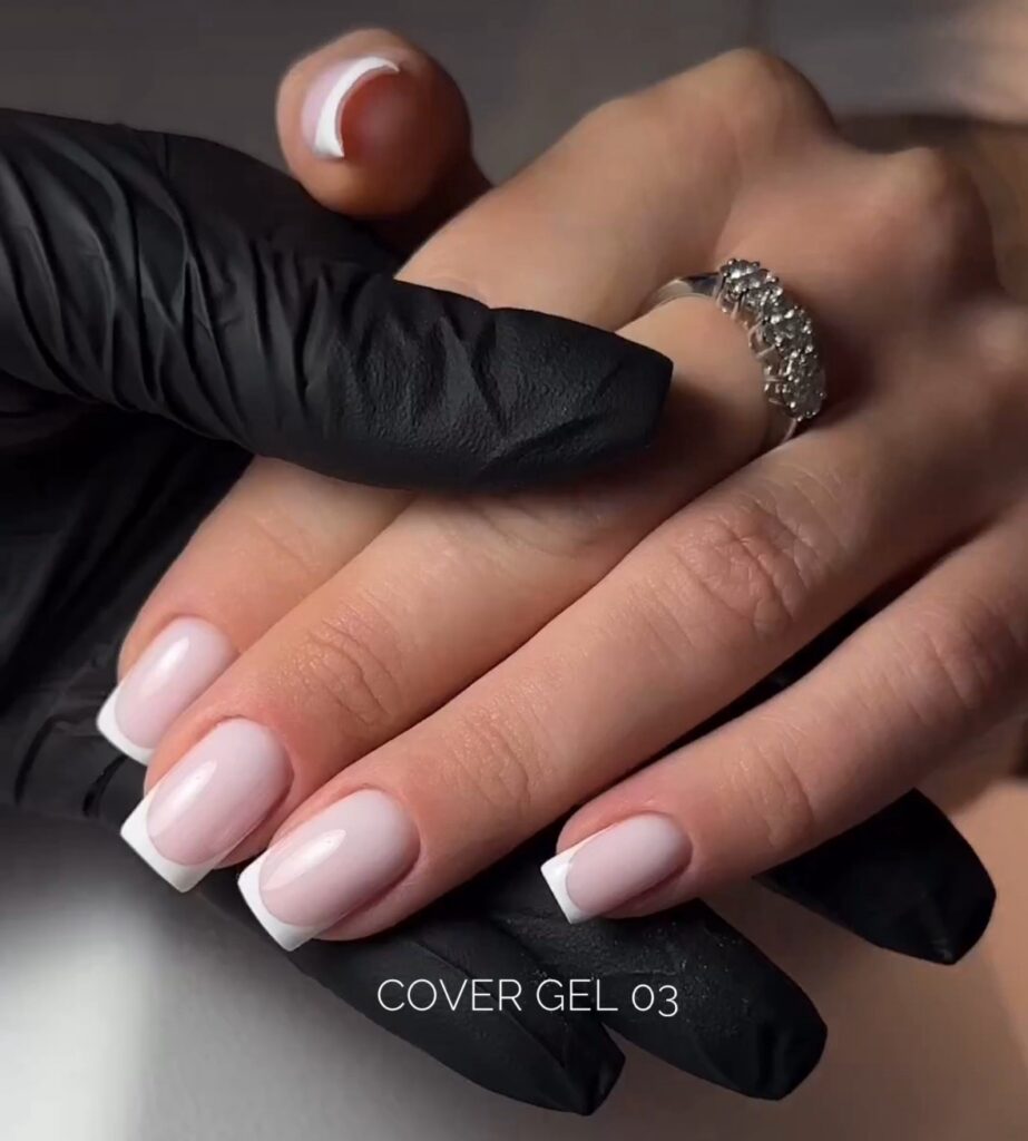 Mano de una clienta con manicura francesa cuadrada sobre el guante negro de la manicurista