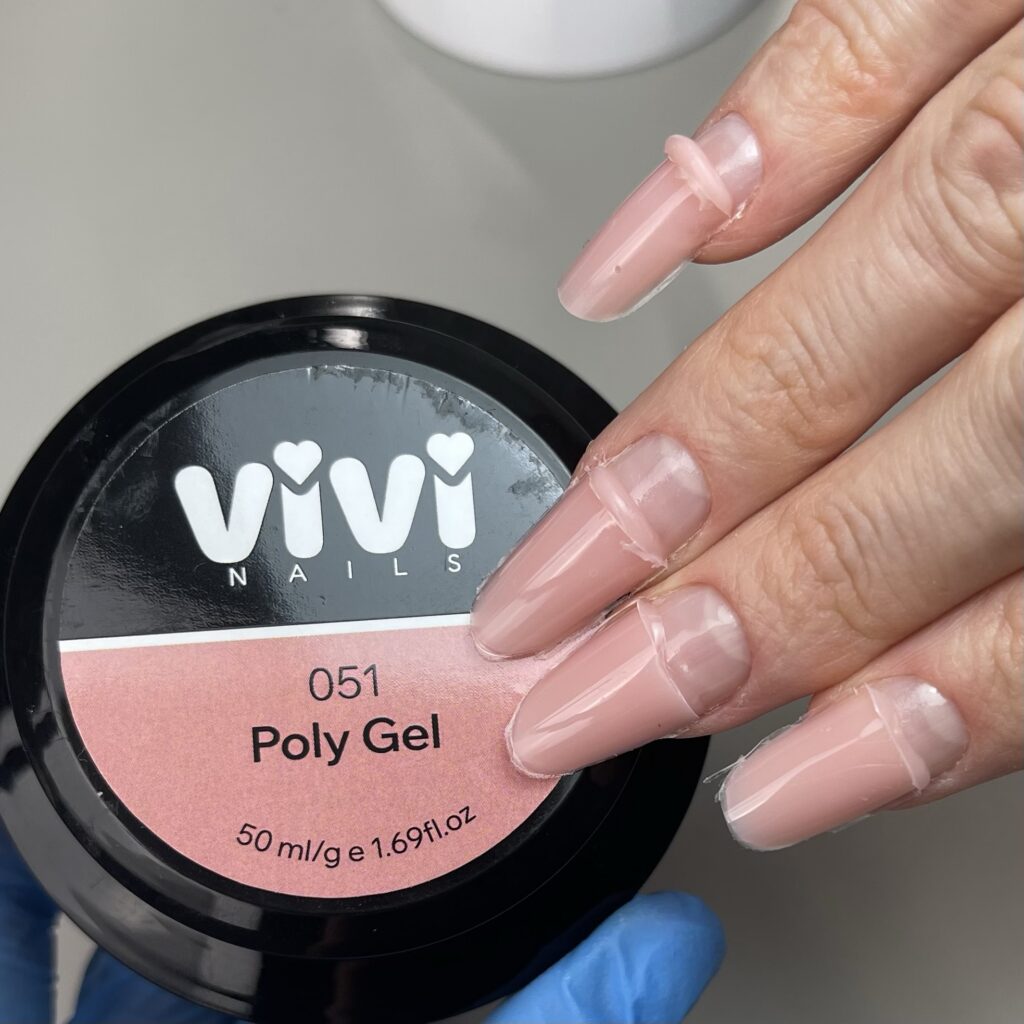 Mano con uñas largas en nude rosado sobre un tarro de polygel Vivi Nails