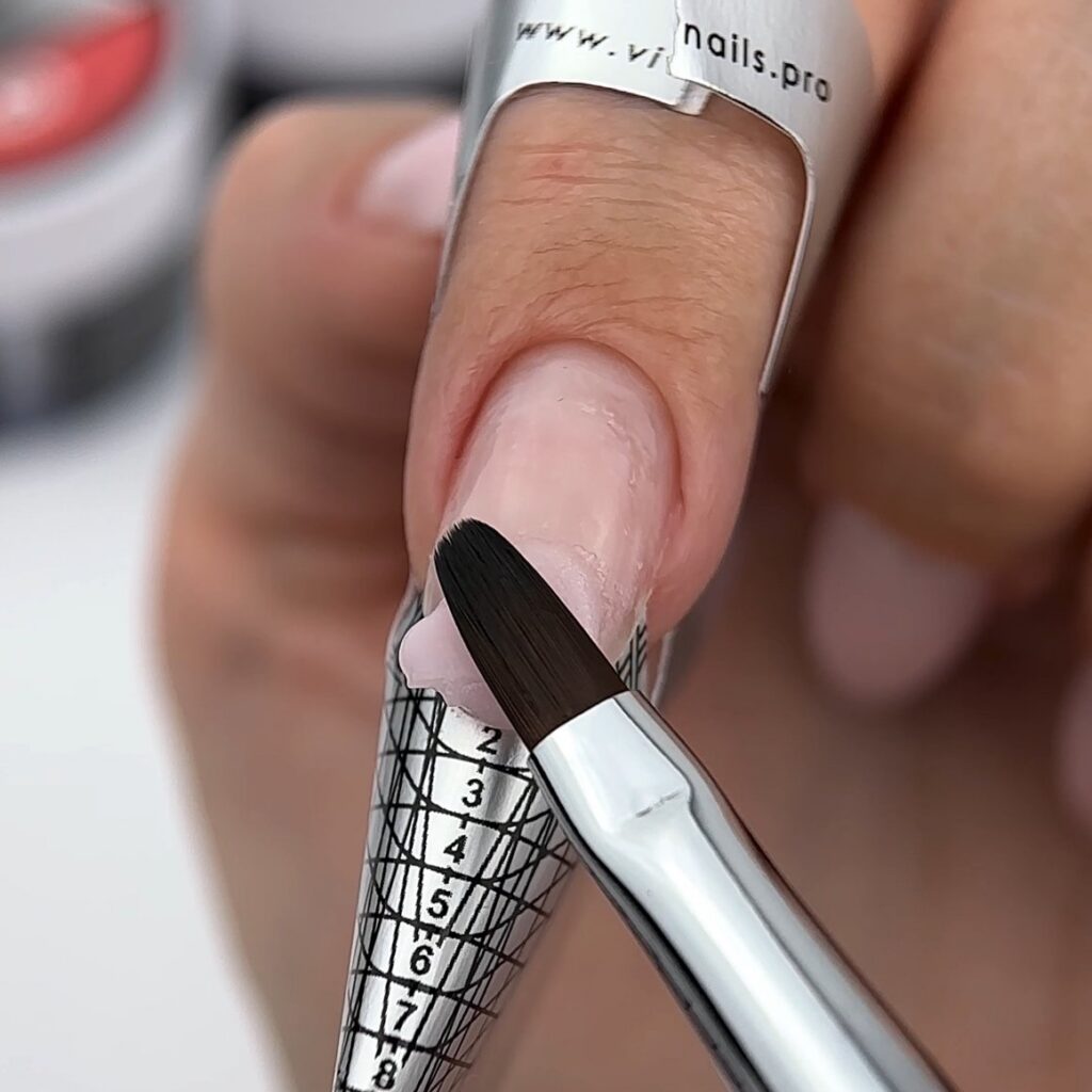 Uña con un molde de extensión colocado y un pincel aplicando gel