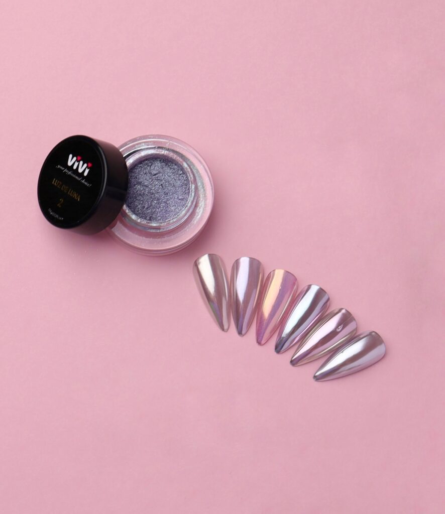 Polvo efecto espejo Luz de Luna Vivi abierto junto a uñas con reflejo perlado plateado y lila