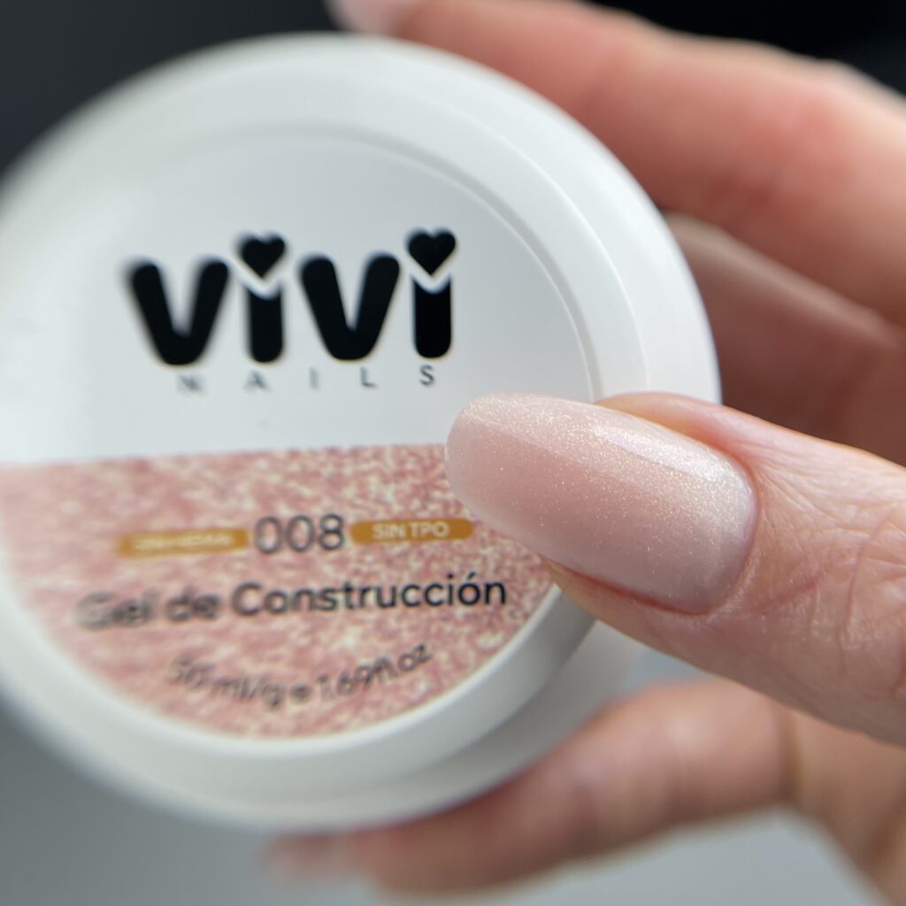 Uña larga en nude con purpurina fina junto al tarro de gel de construcción