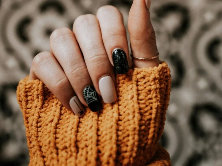 Uñas de Halloween 2026: manicura nude y negra con una telaraña blanca, una araña y una uña negra con purpurina